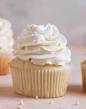 A square image of a vanilla cupcake with vanilla frosting with another in the back left and one to the right.