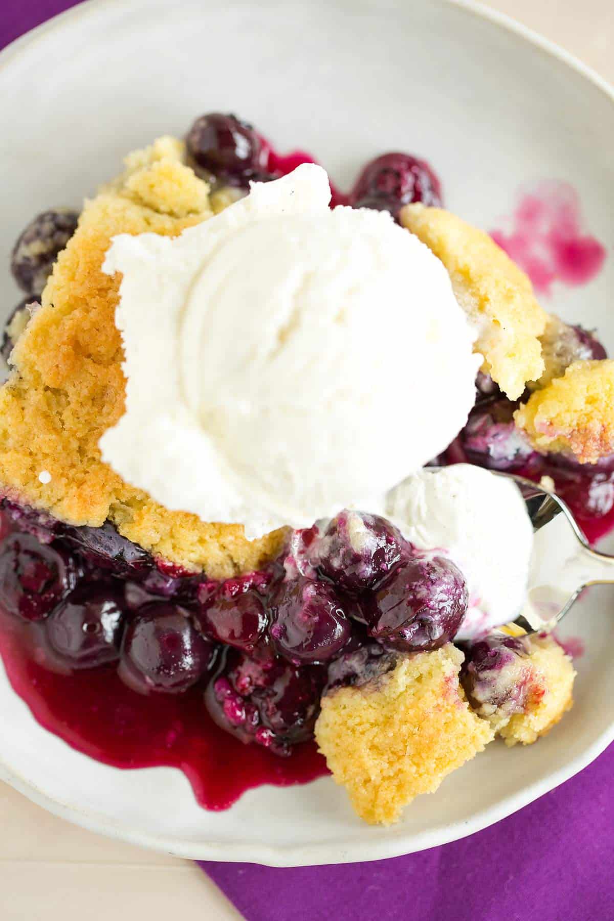 A scoop of blueberry cobbler on a plate with a scoop of vanilla ice cream on top.