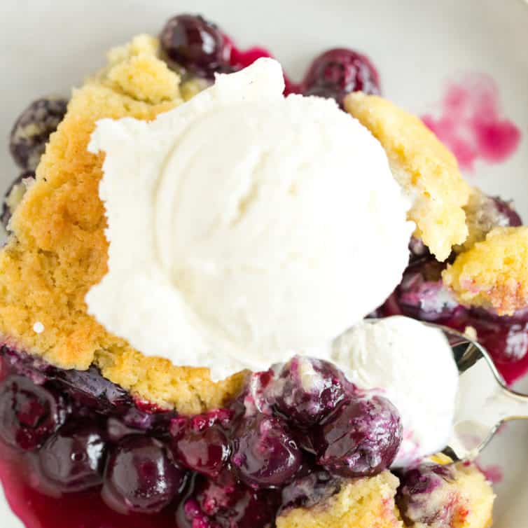 A top down picture of a scoop of ice cream on top of blueberry cobbler in a white bowl.