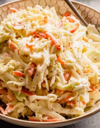 A white bowl with creamy homemade coleslaw and a silver spoon on the right side of the bowl.