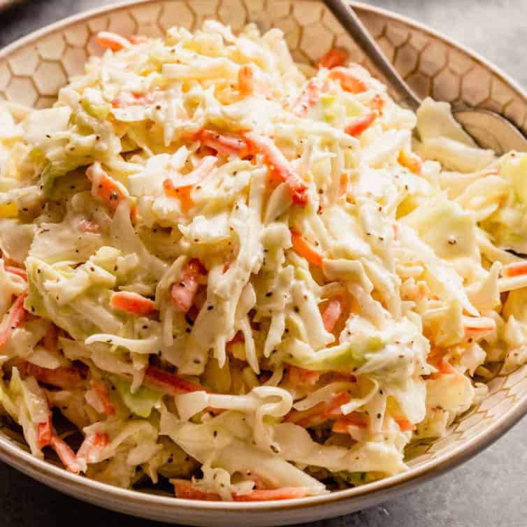 A white bowl with creamy homemade coleslaw and a silver spoon on the right side of the bowl.