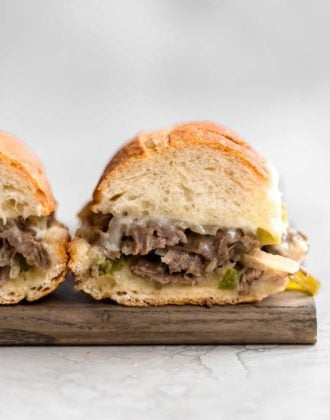 Two philly cheesesteak sandwiches on a wooden cutting board with the insides exposed showing the cheesy meat filling.