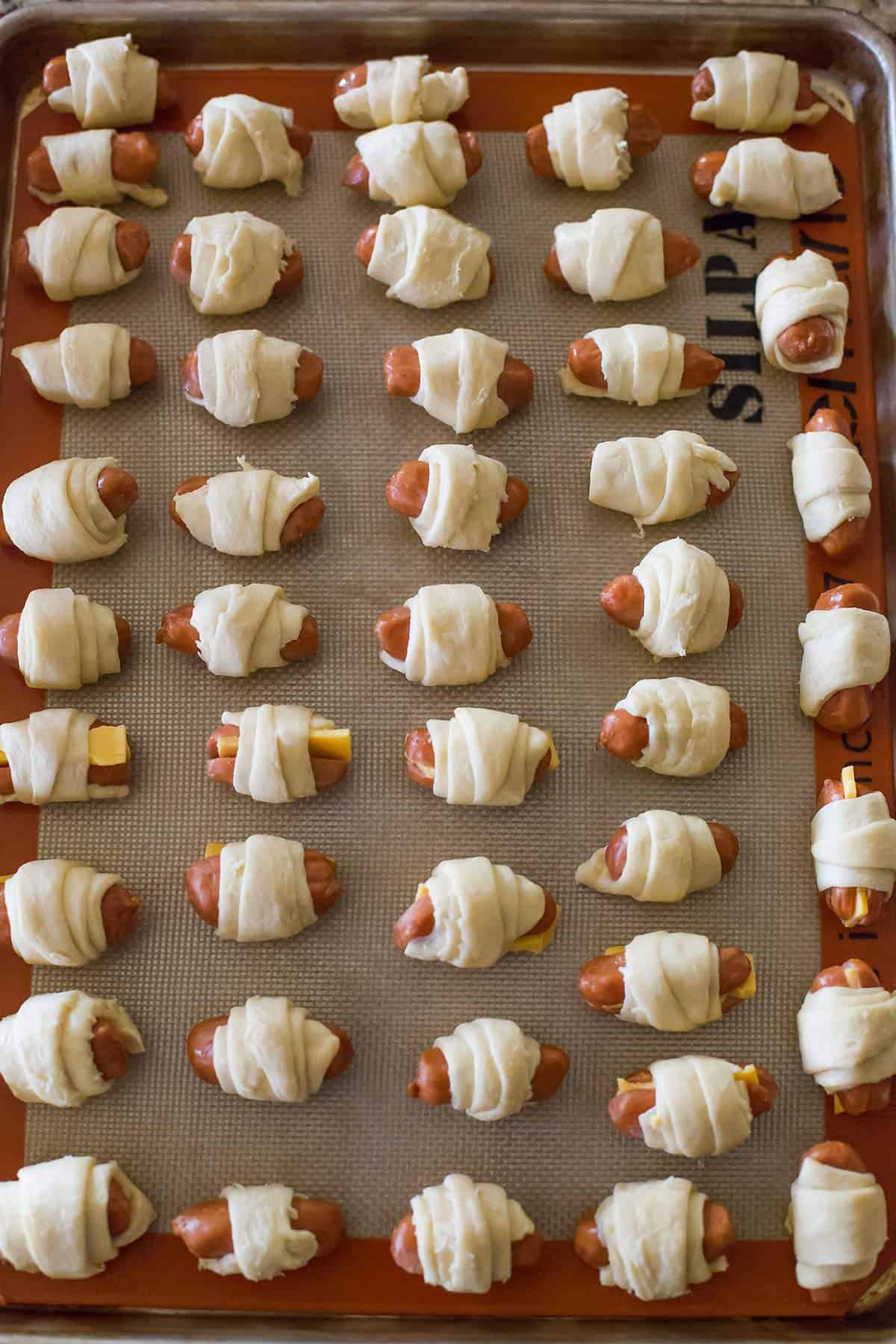 Assembled pigs in a blanket on a baking sheet.