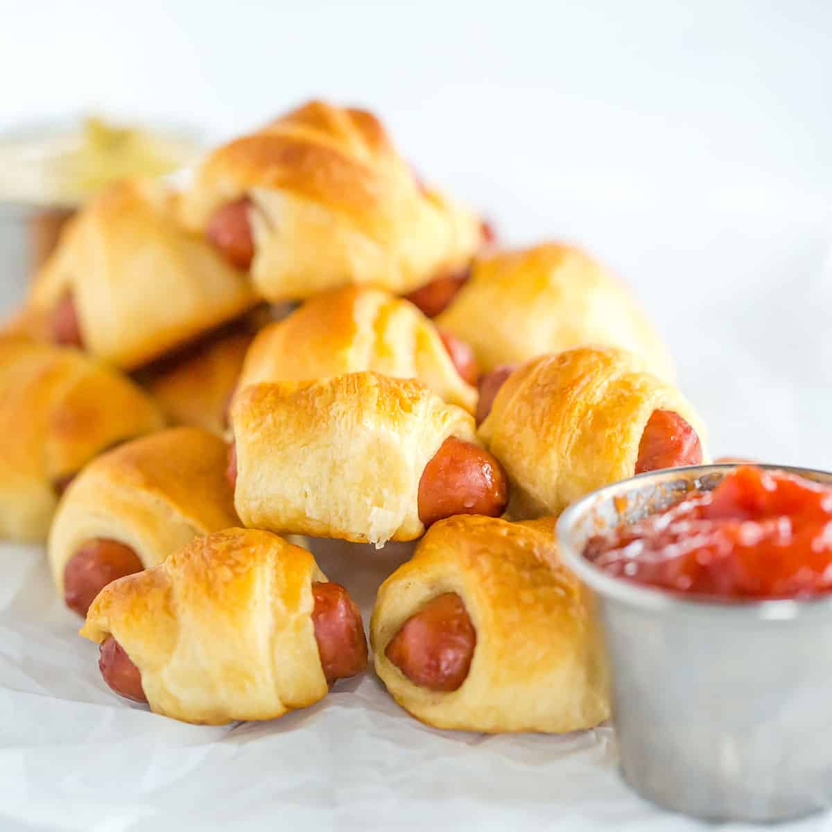 Mini hot dogs wrapped in crescent rolls on parchment paper.