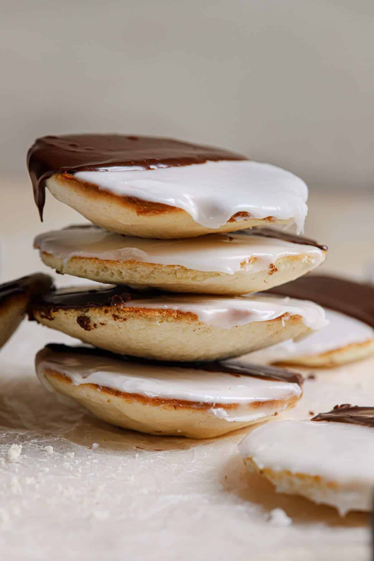 A stack of iced black and white cookies on a counter with a few on the counter below.