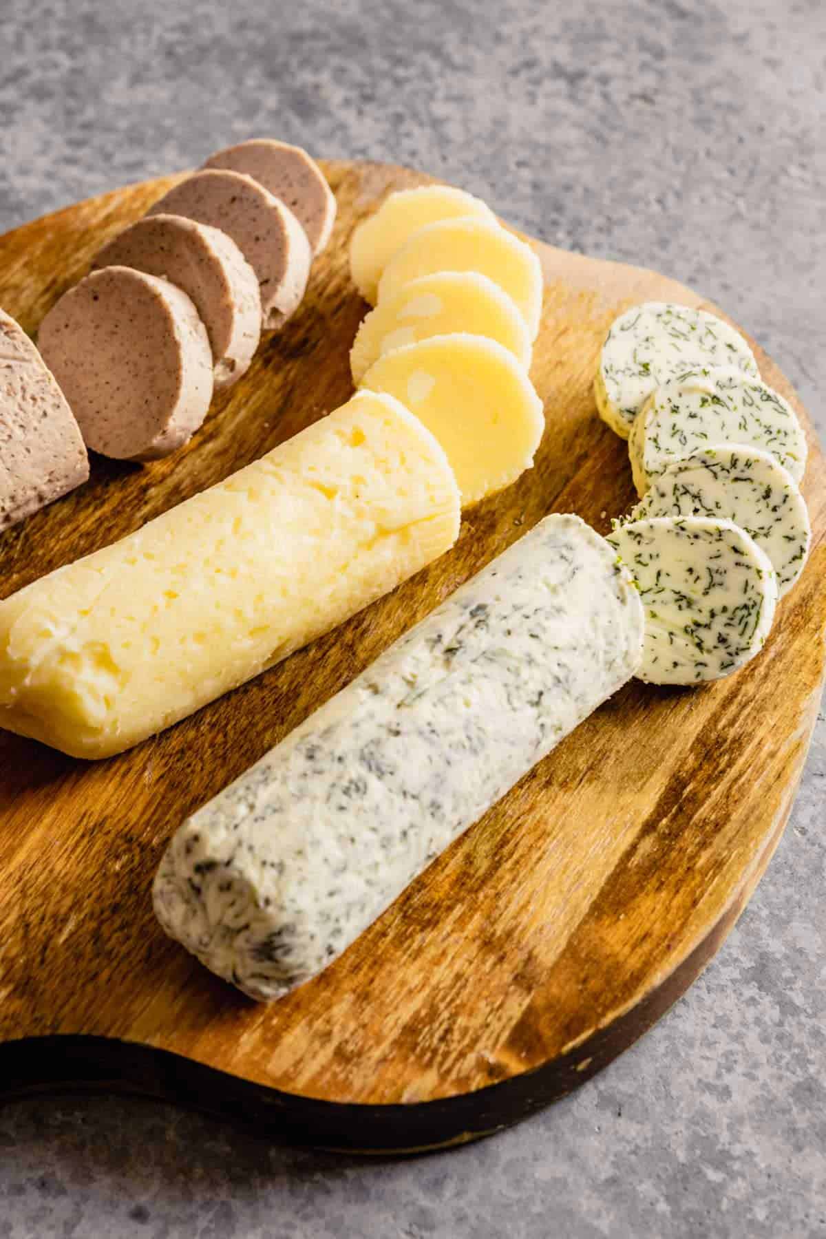 A wooden cutting board topped with three types of compound butter sliced into circles.