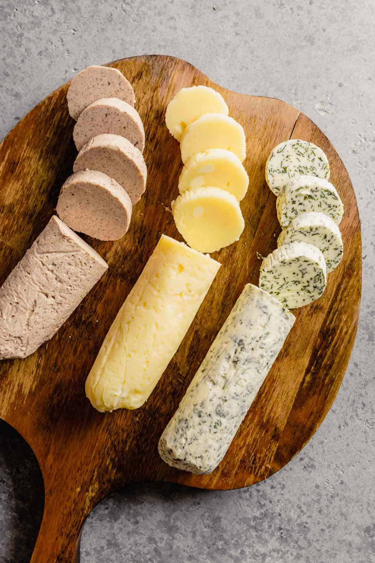 A wooden cutting board with all three types of compound butter on a grey counter.