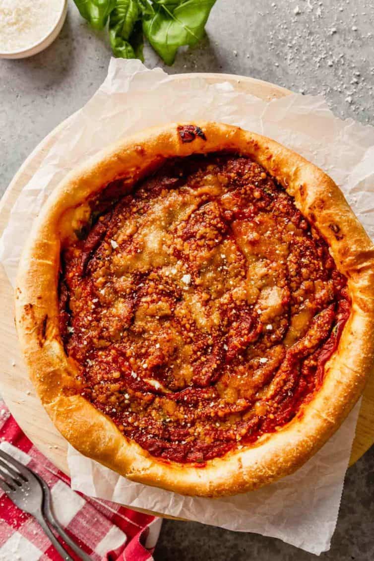 A Chicago-style deep dish pizza on a pizza stone with a fork to the bottom left.