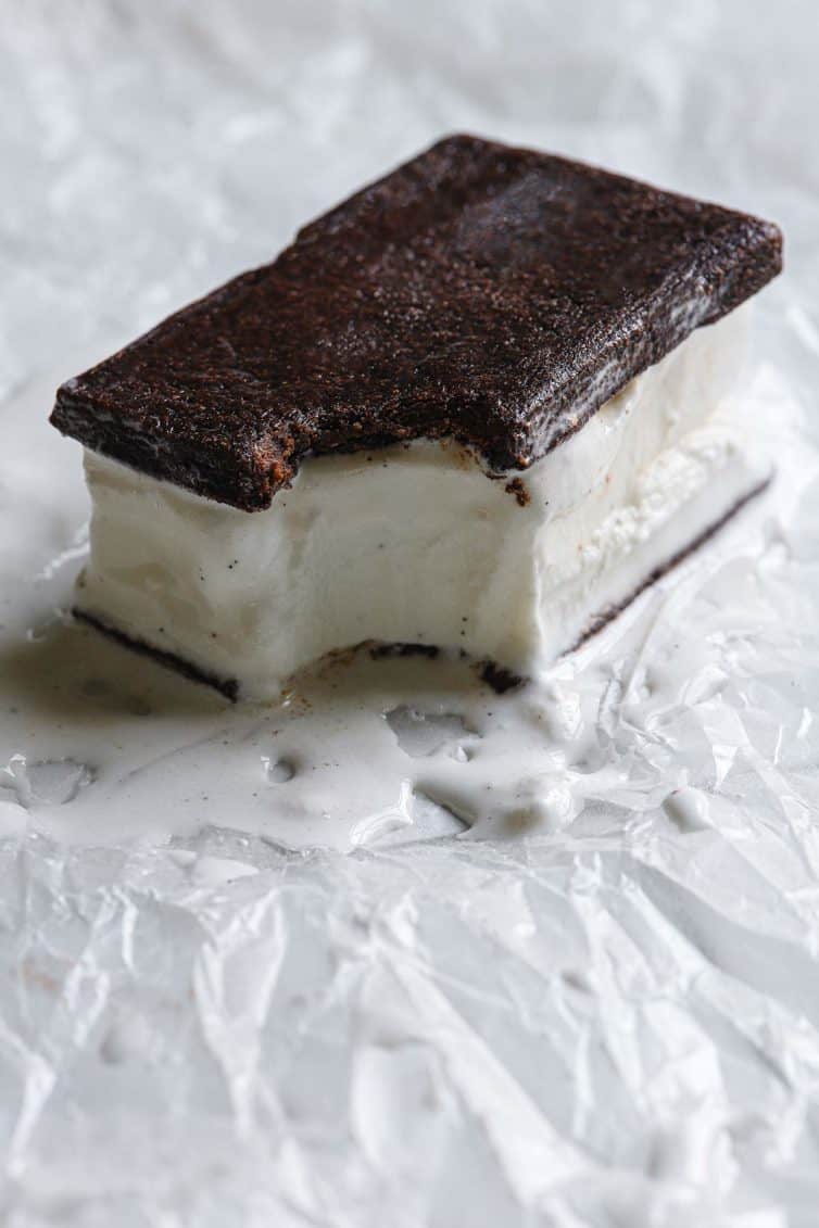 A homemade ice cream sandwich with a bite take out and a little melted on the parchment paper.