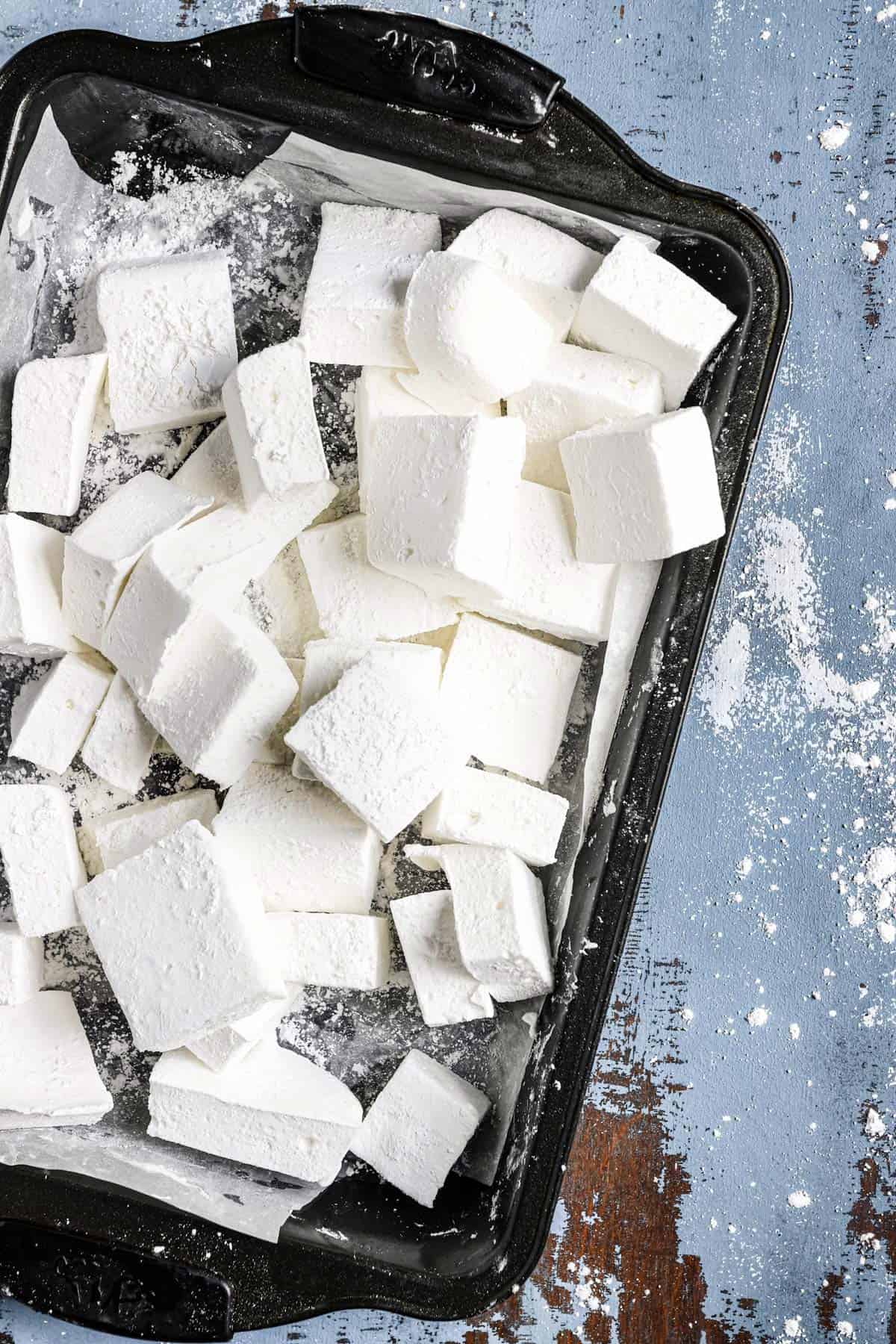 A baking pan lined with parchment paper with cut squares of marshmallow.