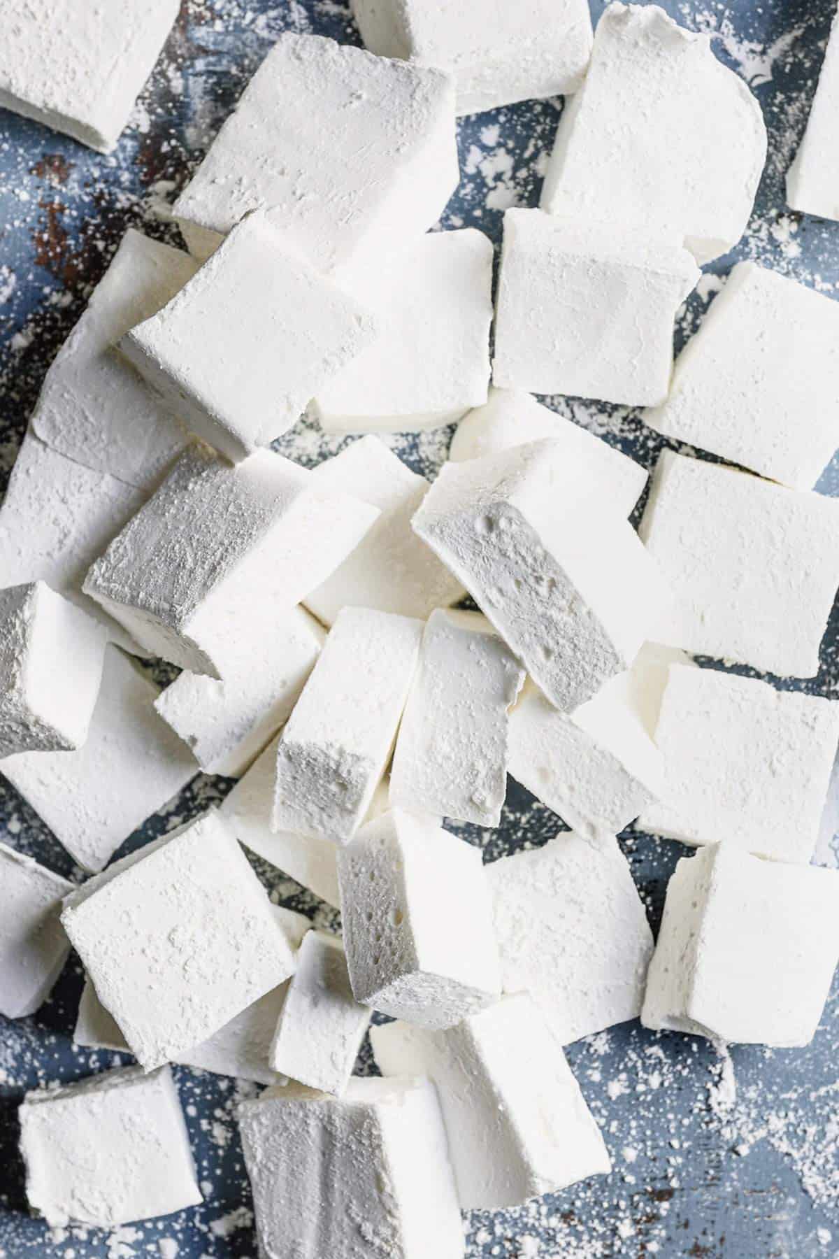 A pile of cut marshmallows on a blue counter dusted with powdered sugar.