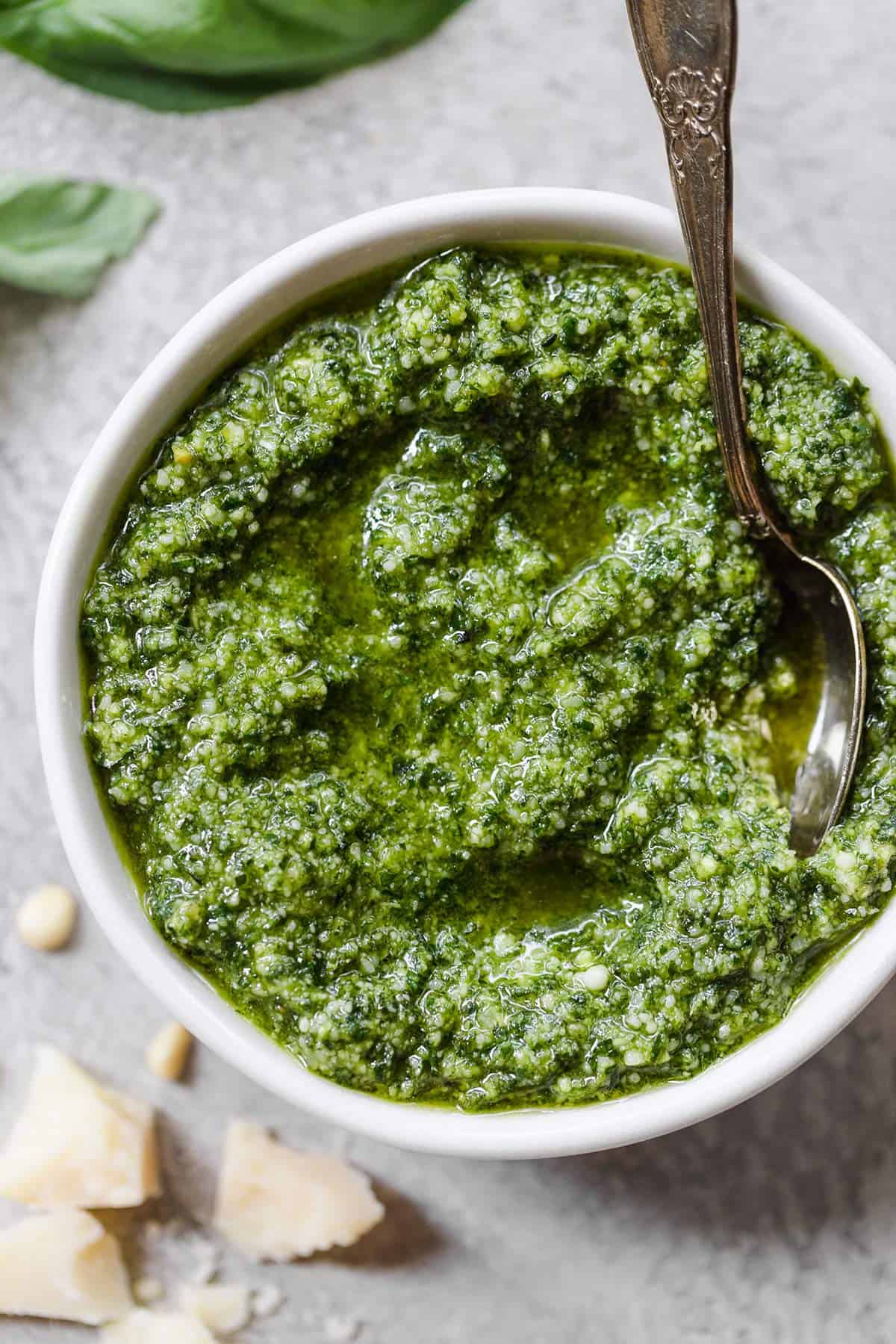 A white bowl with homemade pesto and a silver spoon in the right side of the bowl.