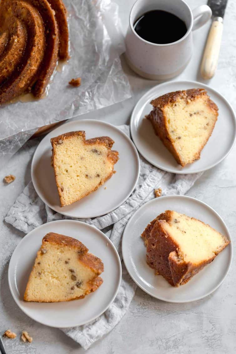 White plates with slices of rum cake on a white counter with a cup of coffee in the back and the rest of the rum cake in the back left corner.