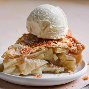 A white plate with a slice of apple pie topped with a large scoop of ice cream on top.
