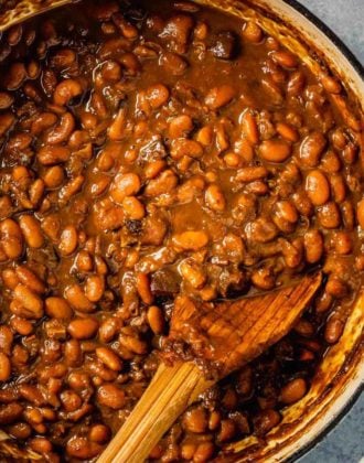 A top down photo of Boston baked beans in a dutch oven with a wooden spoon.