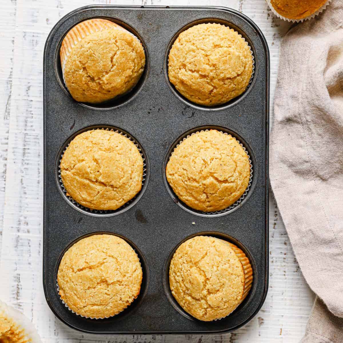 A close up of a non-stick muffin tin with cornbread muffins on a white counter with a light beige towel to the right.