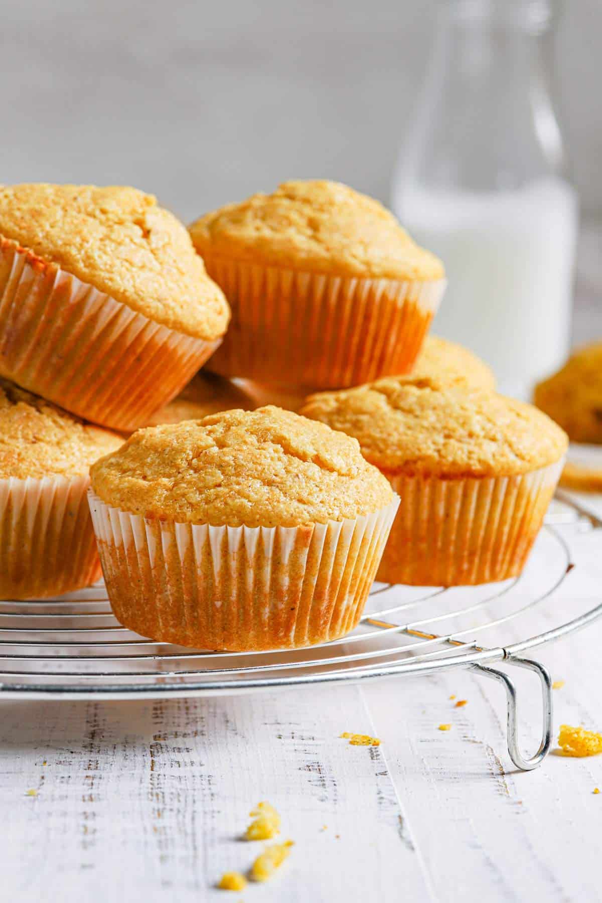 A close up of a pile of cornbread muffins on a wire rack with a jug of milk in the back right.
