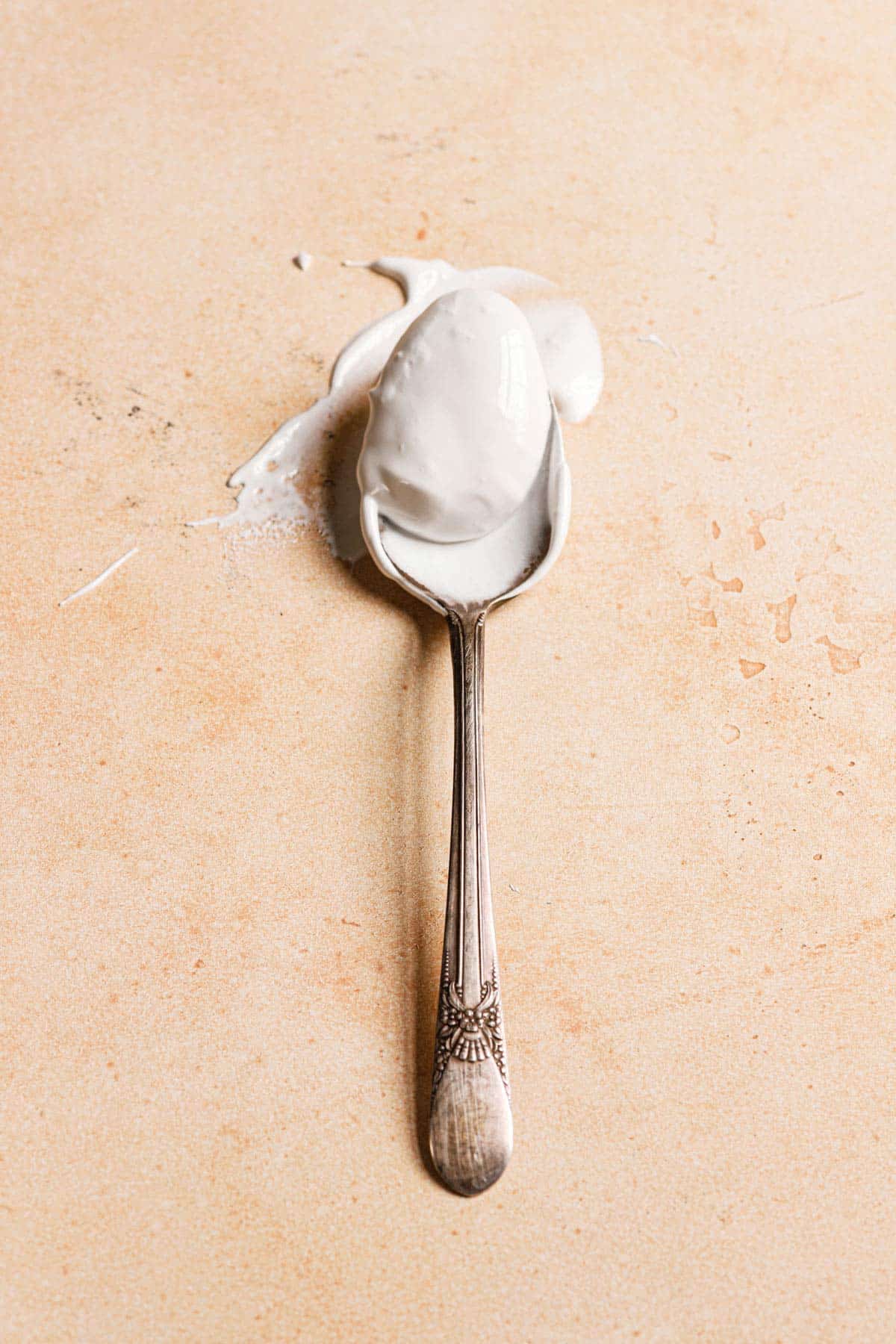 A silver spoon that has been dipped into marshmallow cream on a peach counter.