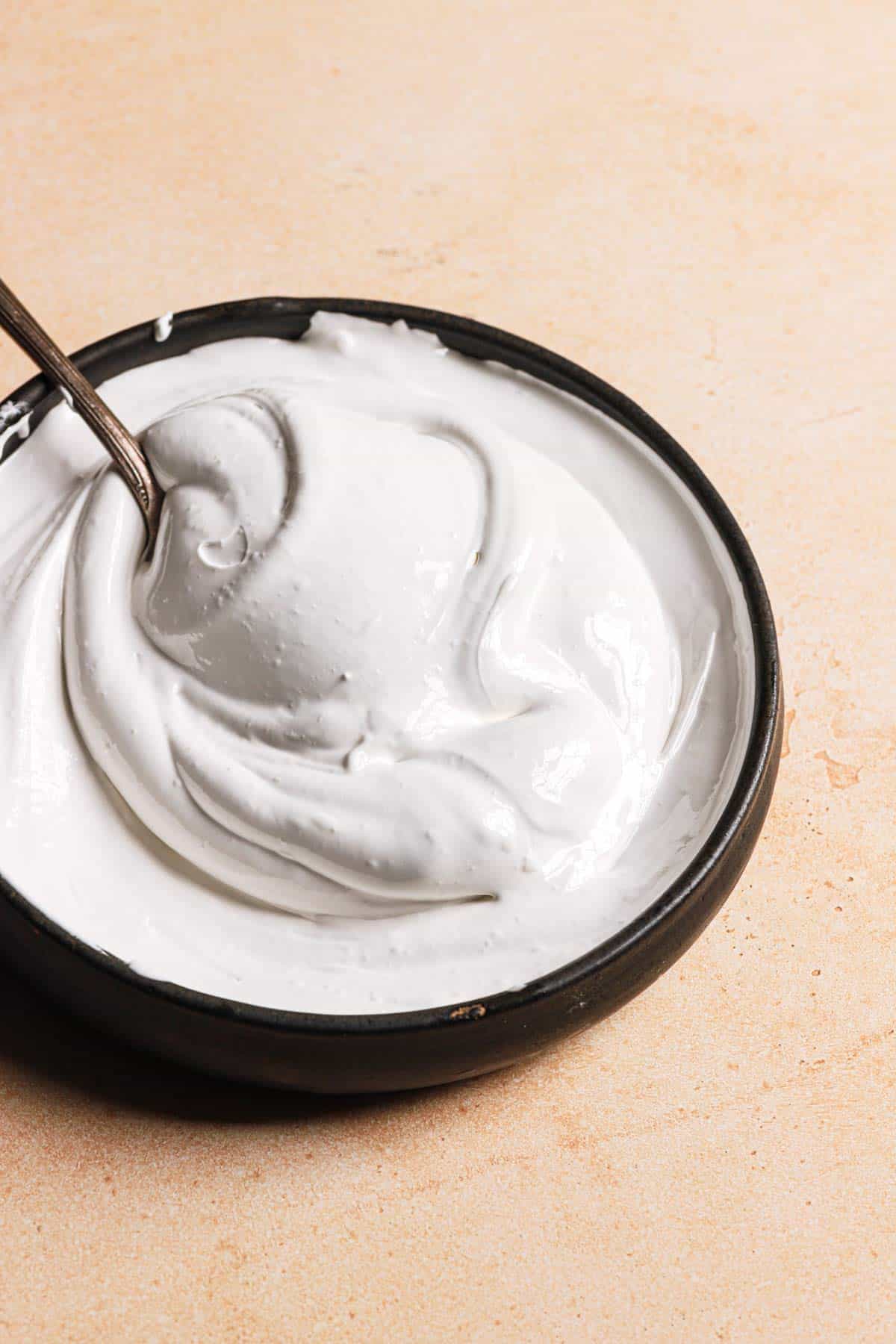 A black bowl filled with marshmallow creme and a silver spoon in the bowl on the left side.