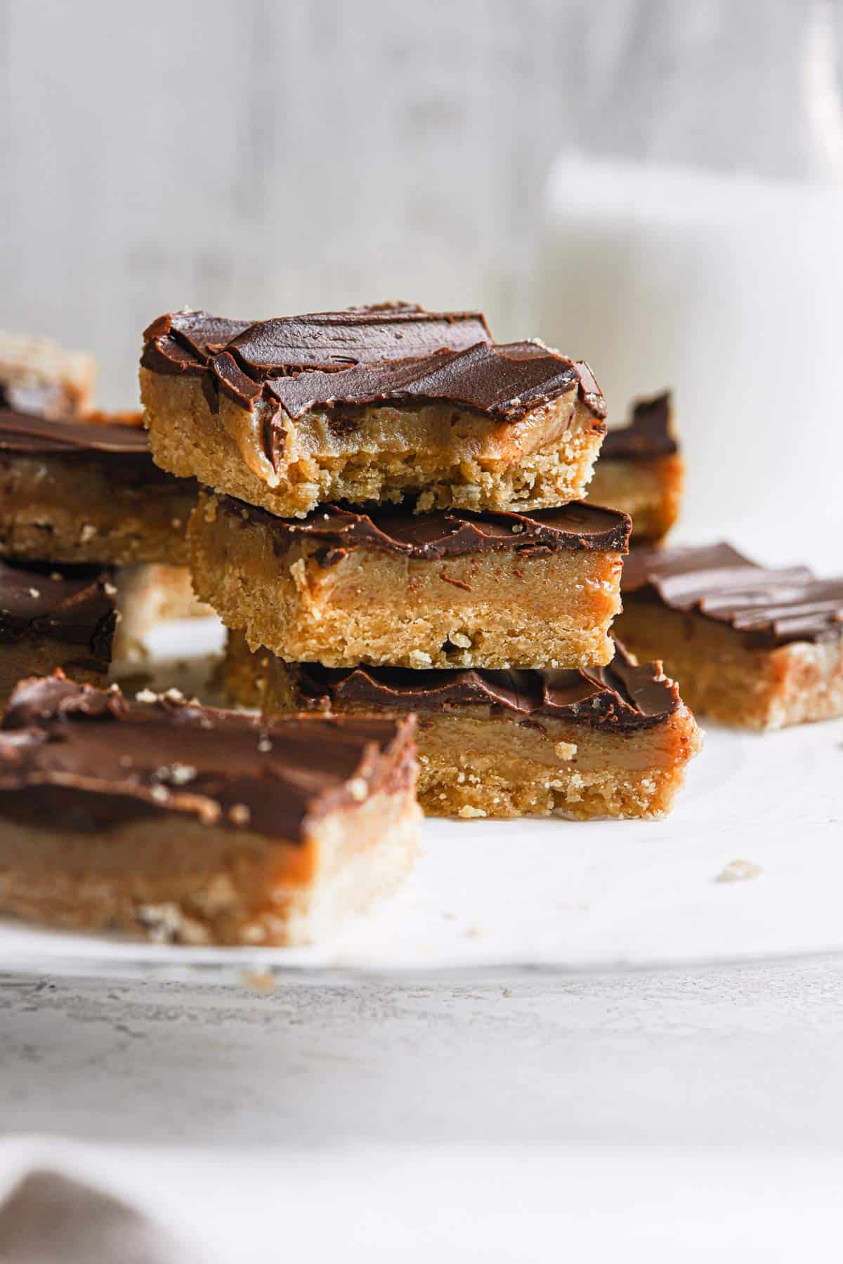 A stack of Millionaire's shortbread bars on a piece of parchment paper with the top bar missing a bite and a jug of milk in the back.