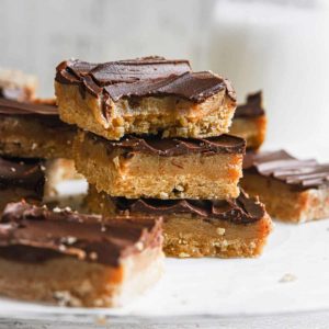 A stack of three millionaire's shortbread bars on parchment paper with the top one missing a bite.