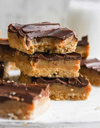 A stack of three millionaire's shortbread bars on parchment paper with the top one missing a bite.