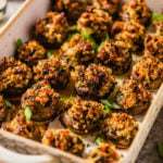 A rimmed baking dish with sausage stuffed mushrooms garnished with green onion.