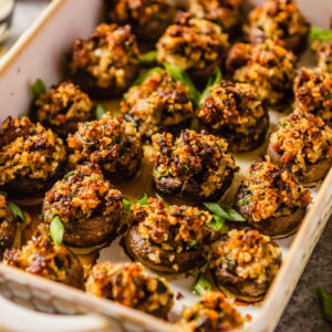 A rimmed baking dish with sausage stuffed mushrooms garnished with green onion.