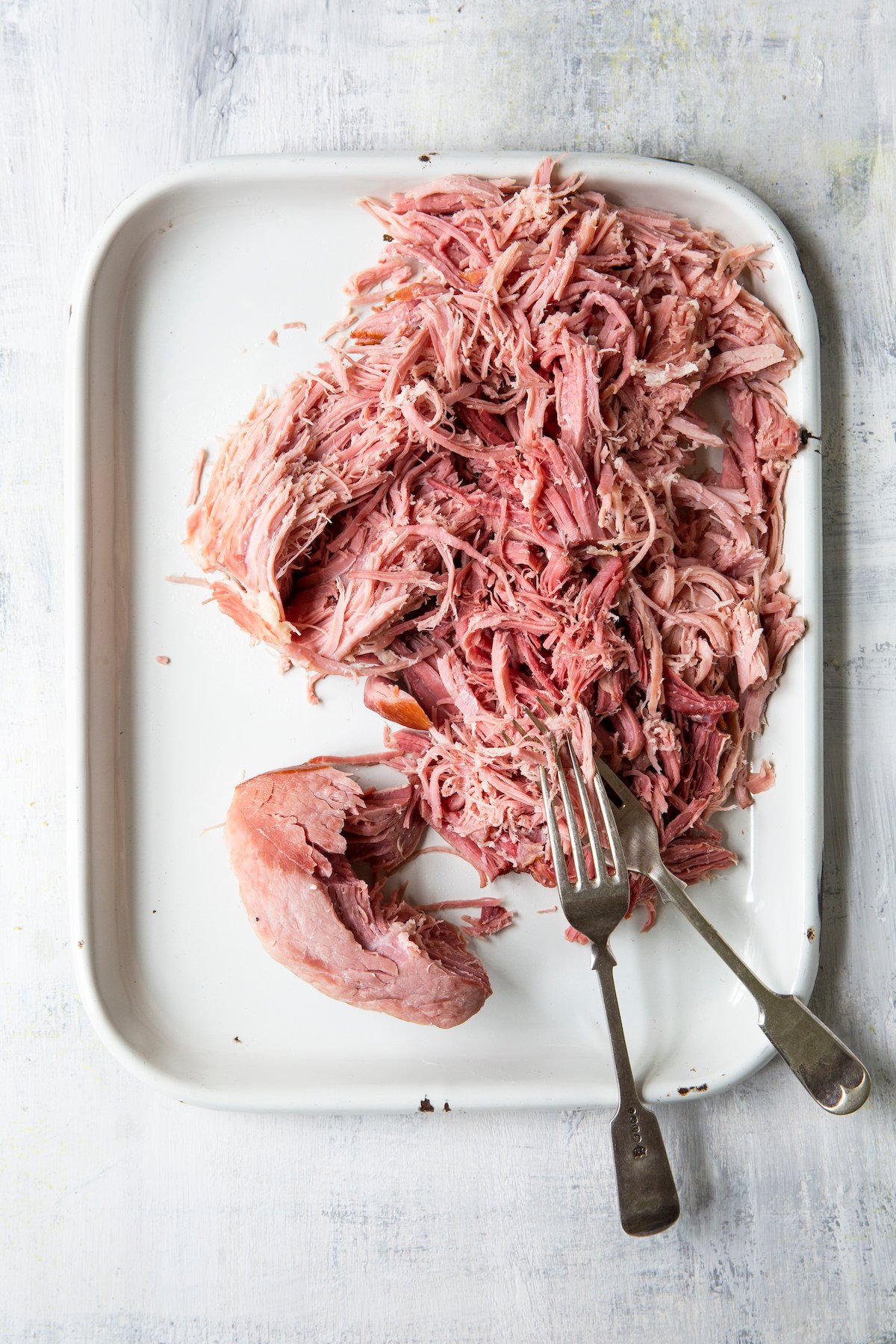 Overhead shot of ham being shredded on platter with two forks