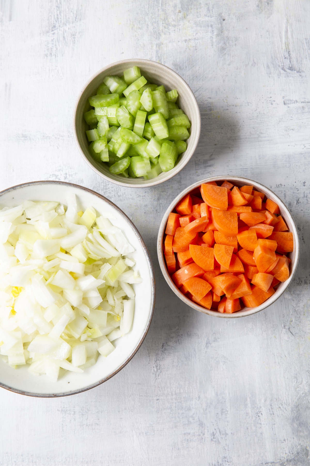 Overhead shot of onions, carrots, and celery in bowls