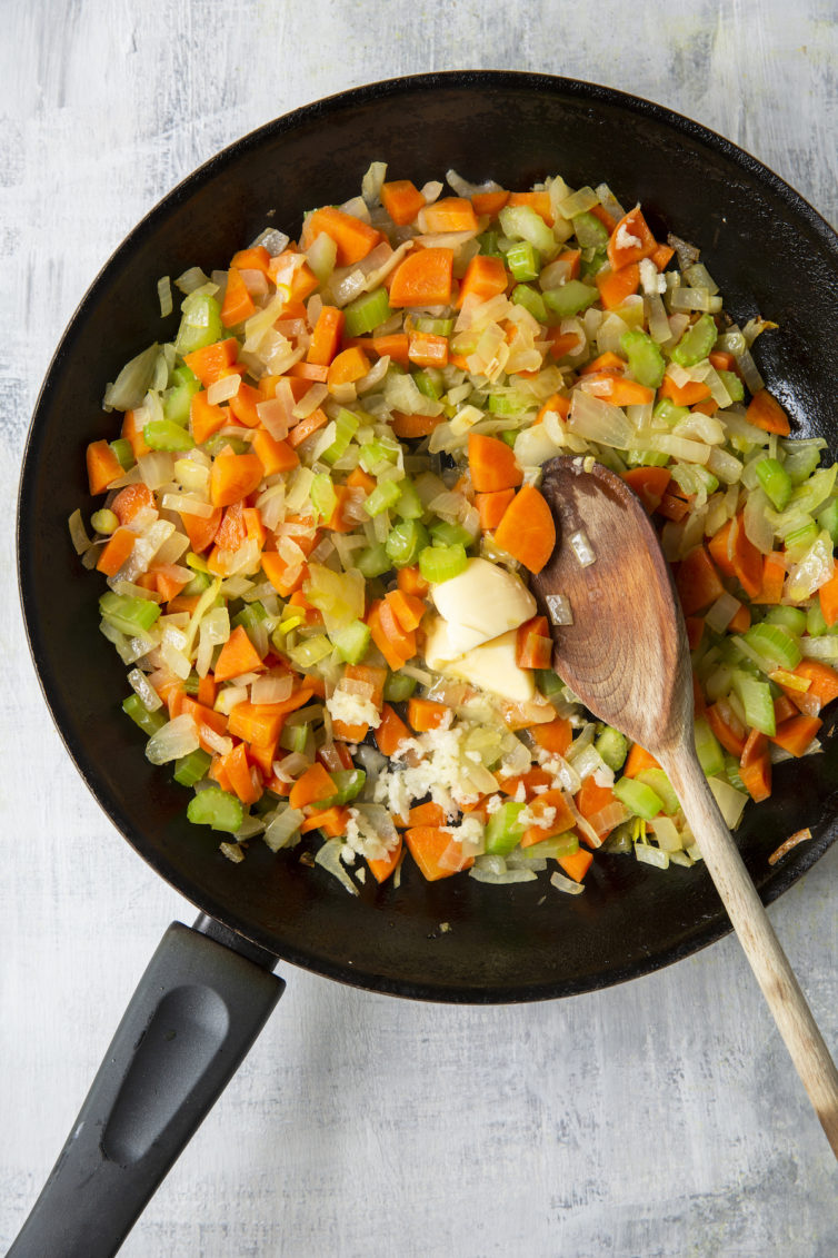 Onions, celery, and carrots in skillet with wooden spoon
