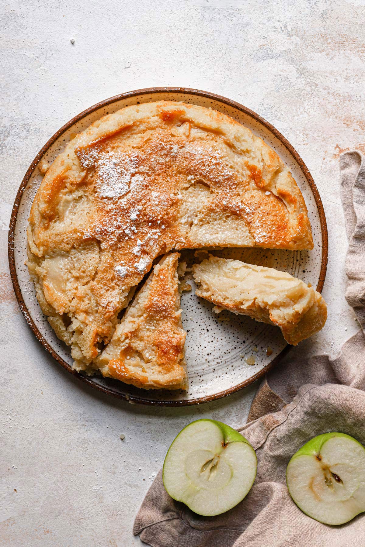 French apple cake on a round serving plate with one slice cut away and on its side.