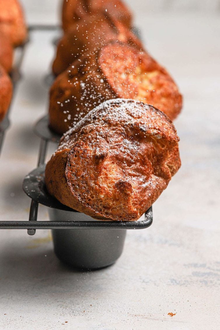 Golden brown baked breakfast popovers in a grey popover baking pan dusted with powdered sugar