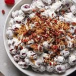 a large white serving bowl filled with this homemade grape salad recipe topped with brown sugar and chopped toasted pecans