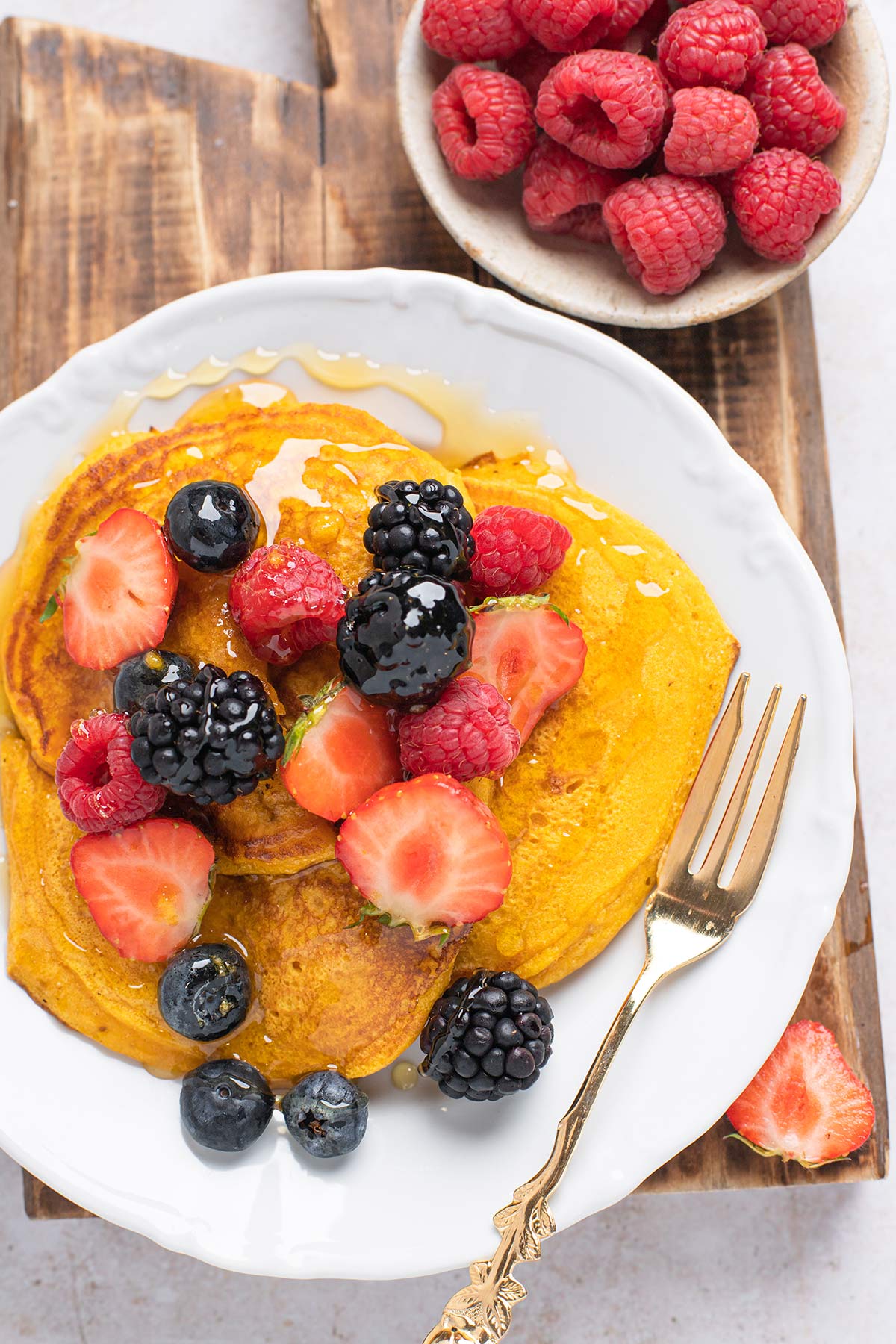 Plate of pumpkin pancakes with berries on top and drizzled with syrup.