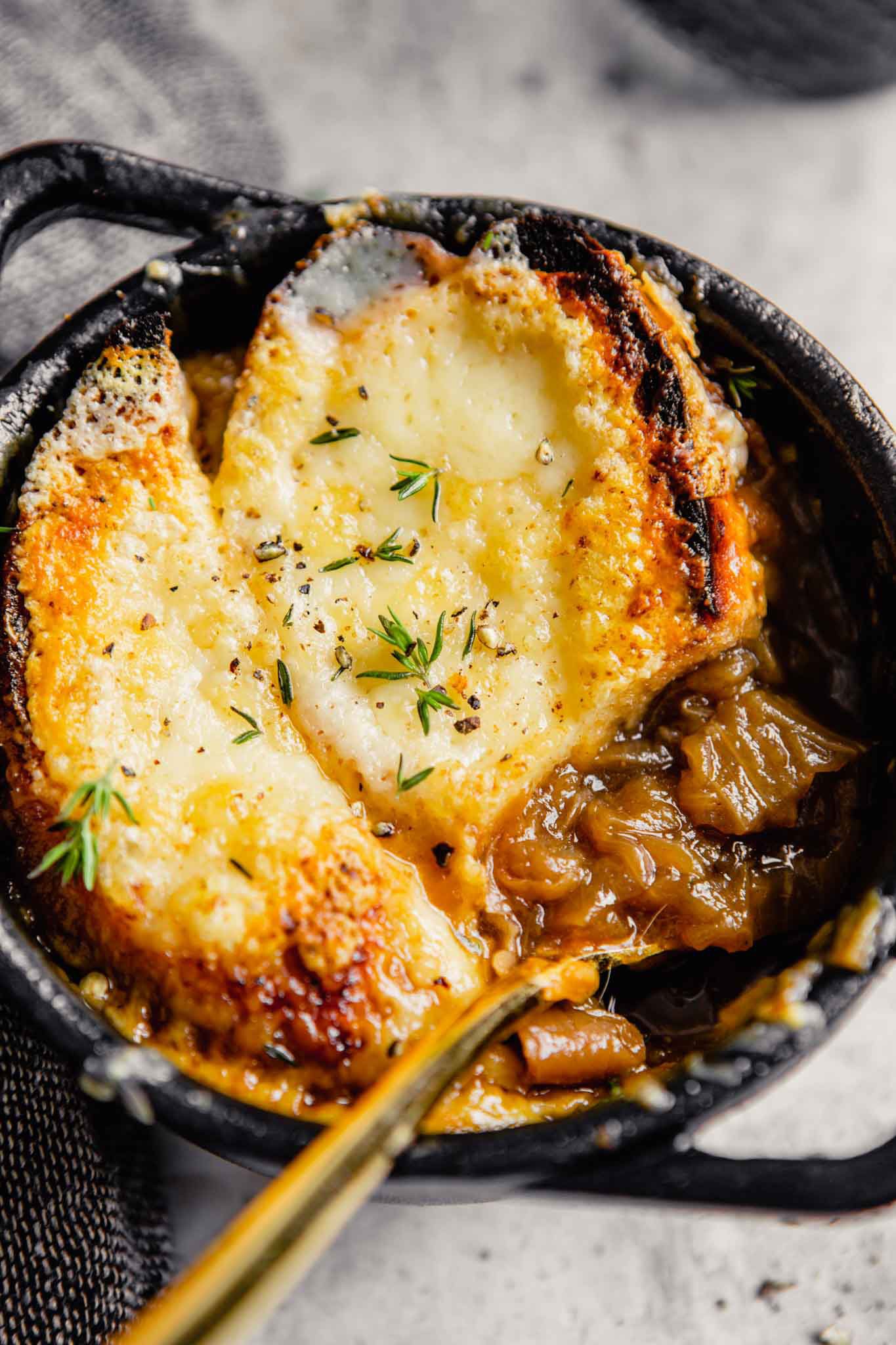 A bowl of French onion soup with a spoon scooping out onions.