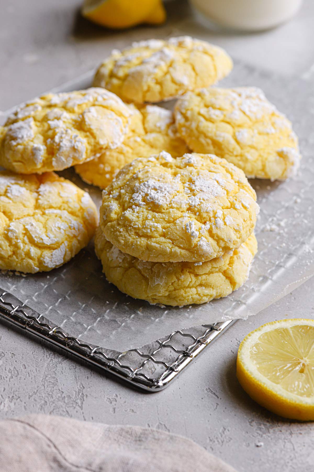 a few lemon crinkle cookies resting on a wire cooling rack with a lemon slice off to the right-hand side