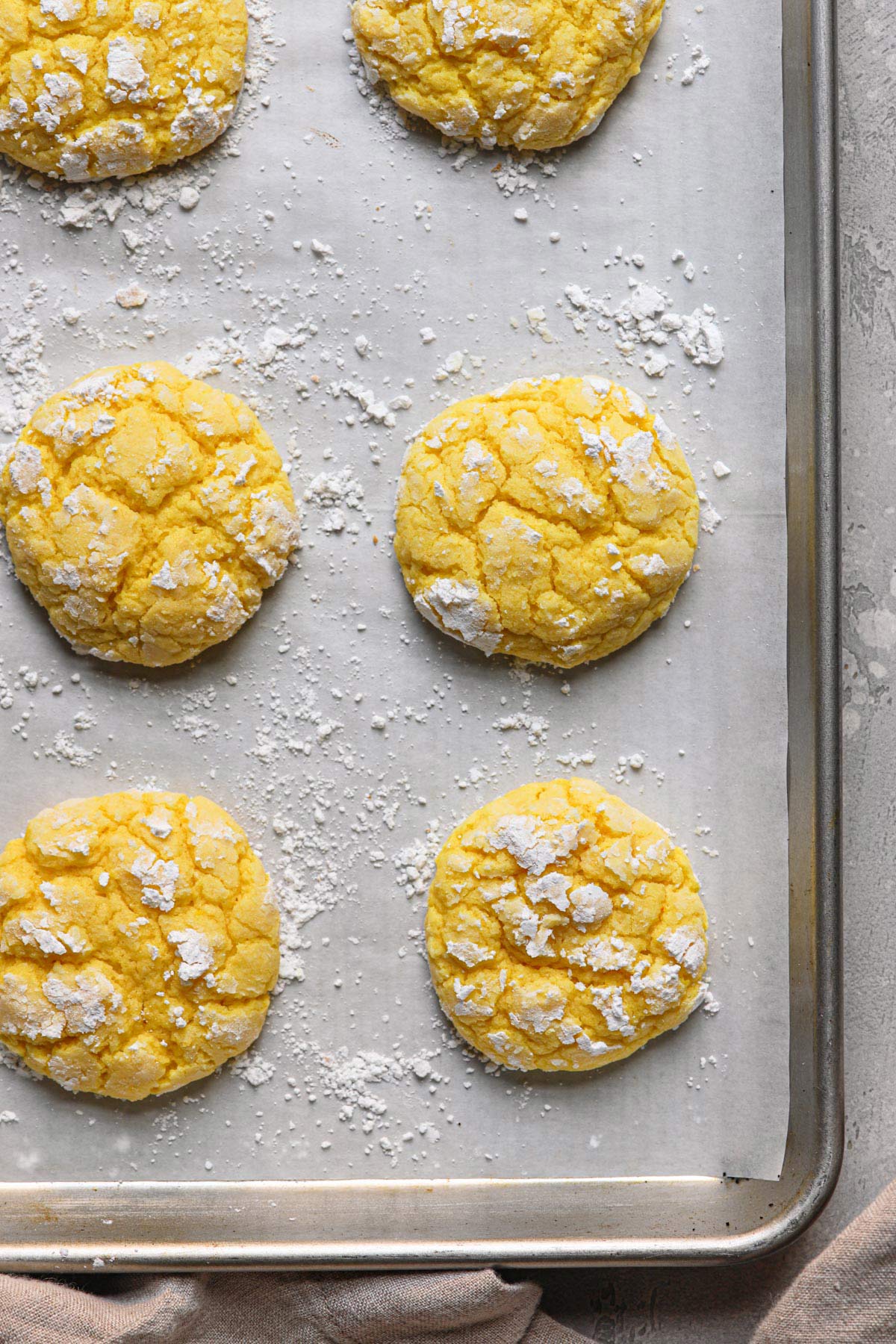 a few lemon crinkle cookies resting on a lined baking sheet dusted in powdered sugar