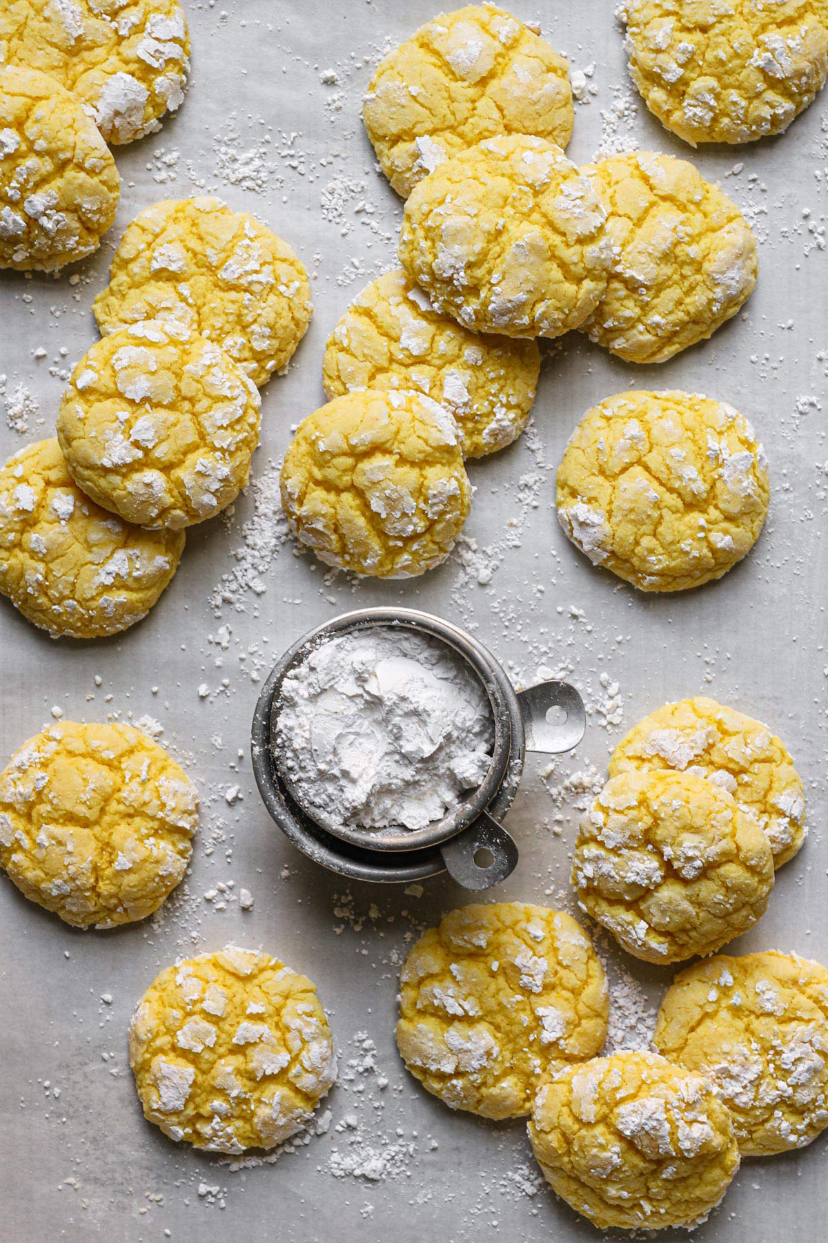 a few lemon crinkle cookies resting on a lined baking sheet dusted in powdered sugar with a small bowl of powdered sugar in the center