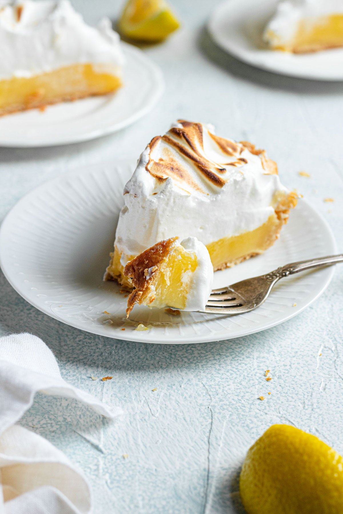 A slice of lemon meringue pie on a white plate with a fork.