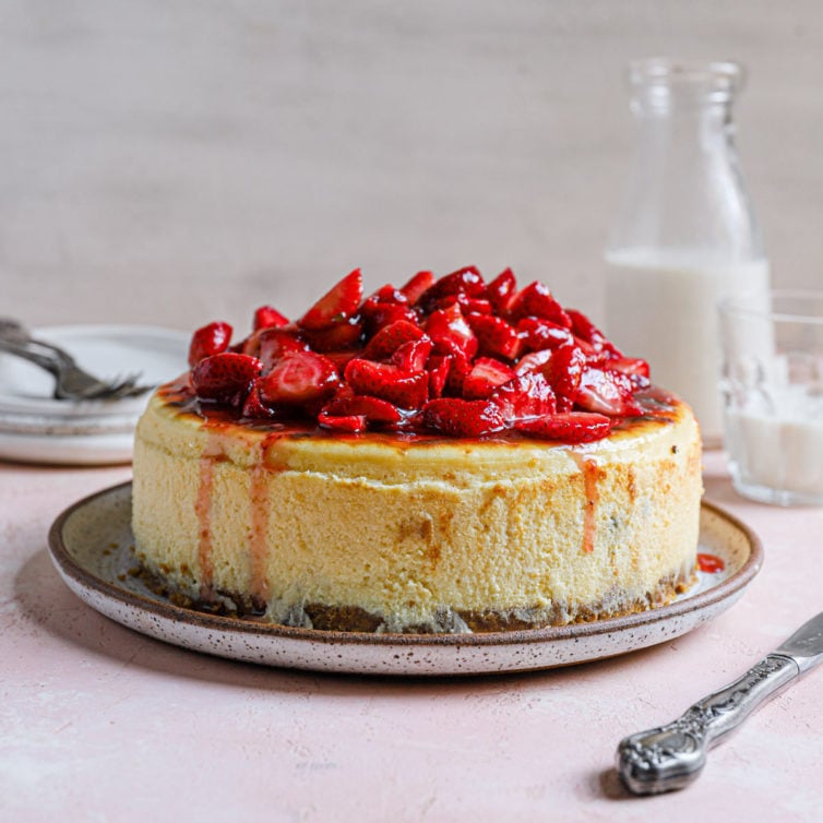 New York cheesecake topped with fresh strawberry sauce on a serving plate.