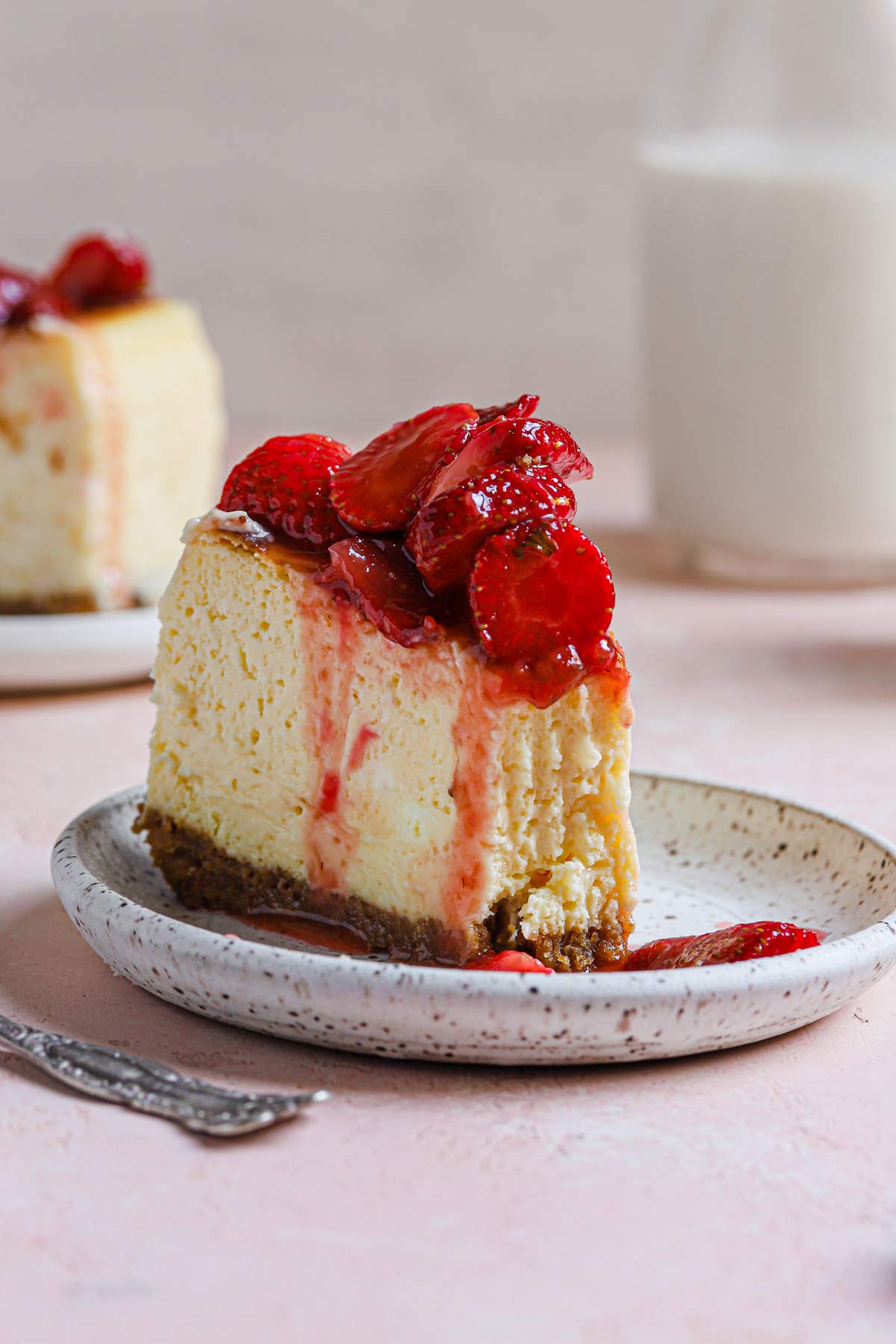 Slice of New York cheesecake with fresh strawberry topping on a plate.