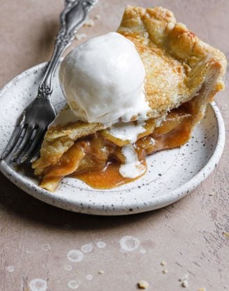 a slice of this salted caramel apple pie served on a stoneware plate with vanilla ice cream