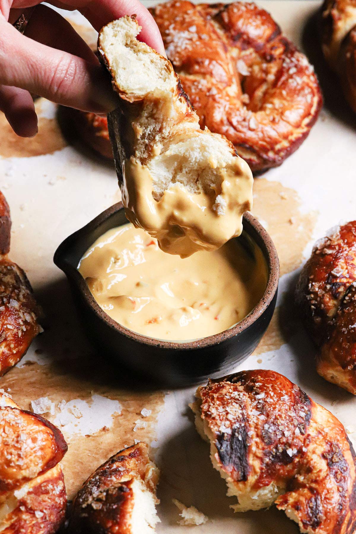 A piece of soft pretzel being dipped into a beer cheese sauce