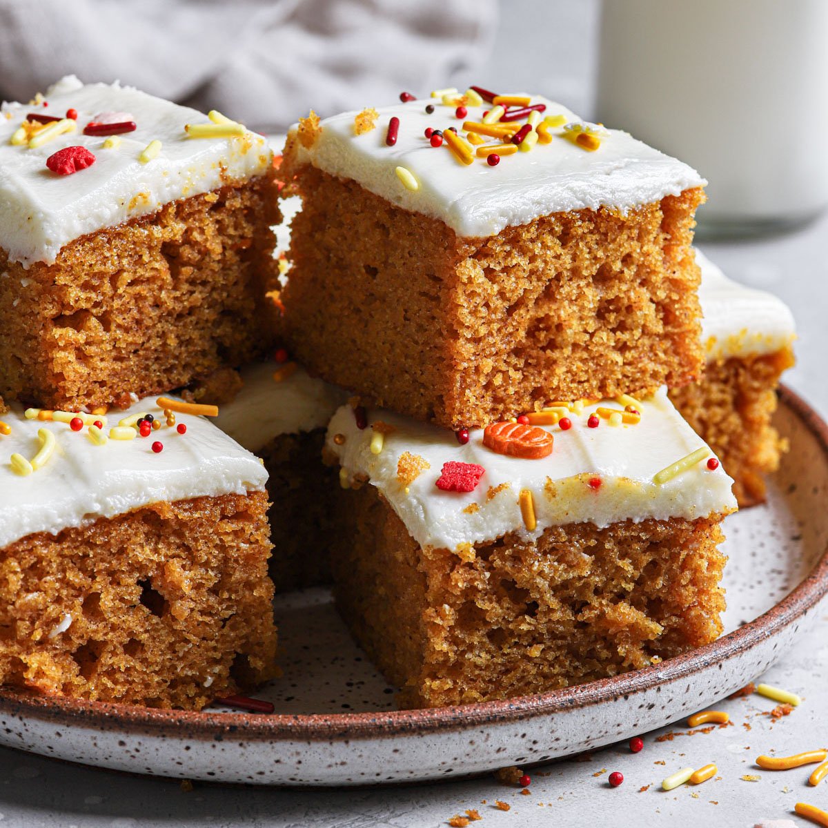 Squares of pumpkin bars stacked on a flecked gray plate.