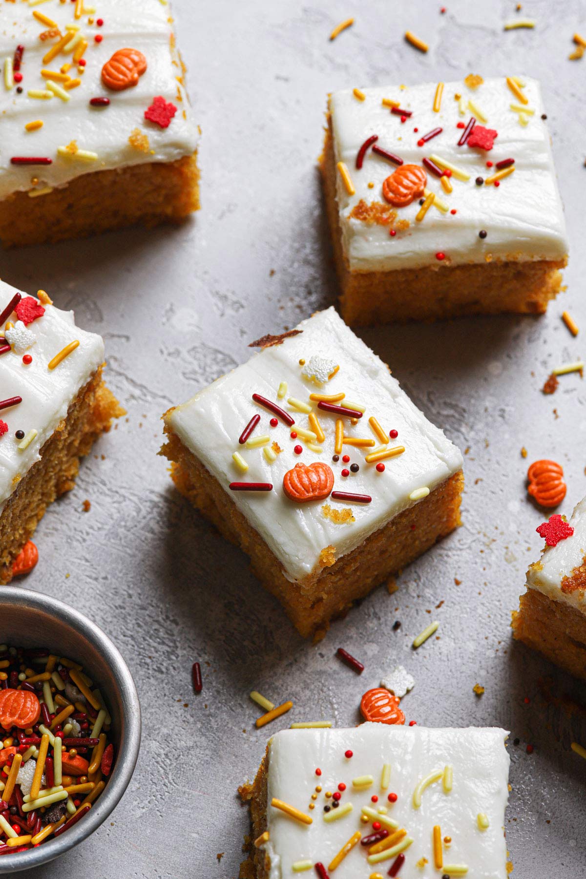 Squares of pumpkin bars with fall and pumpkin sprinkles on top and around surface.