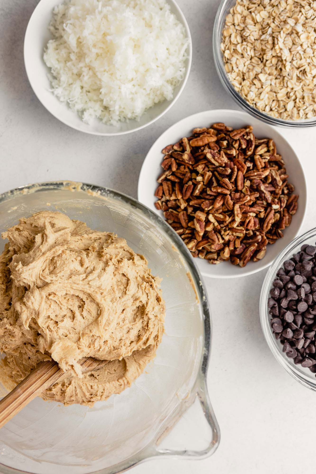 Cookie dough in a glass bowl with mix-ins in prepped bowls next to it.