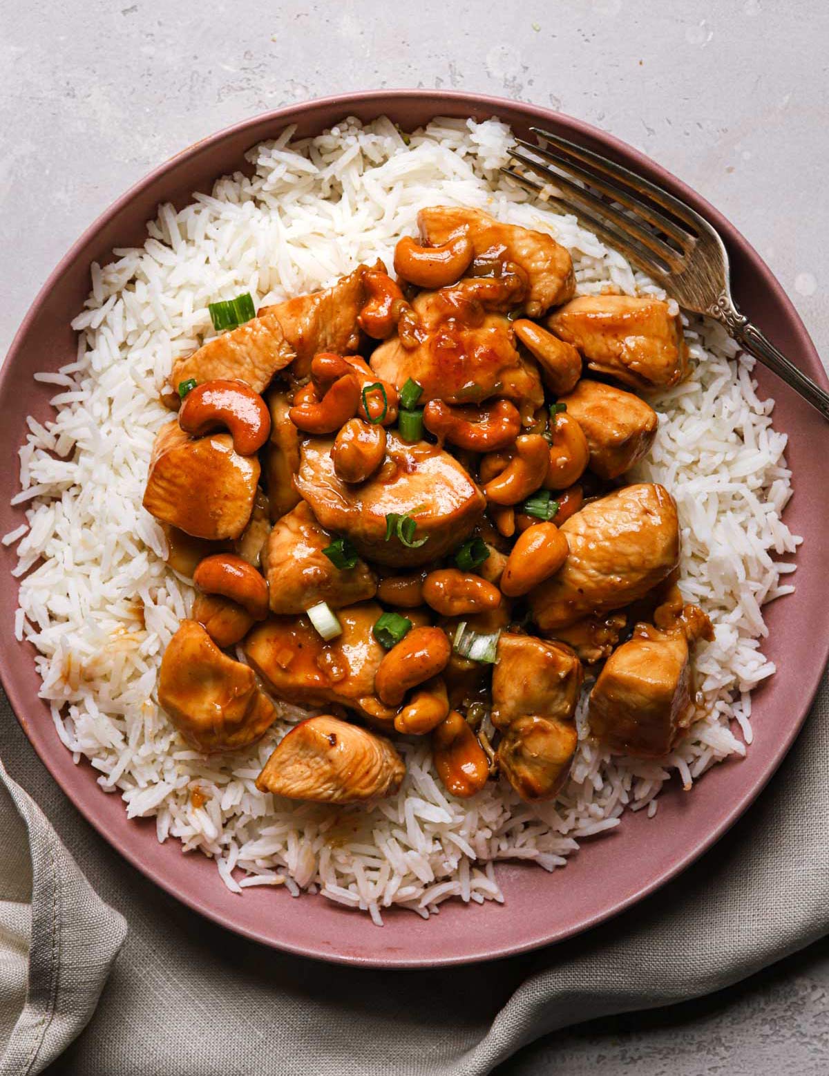 Stir-fried cashew chicken over white rice on a pink plate with a fork on the side.