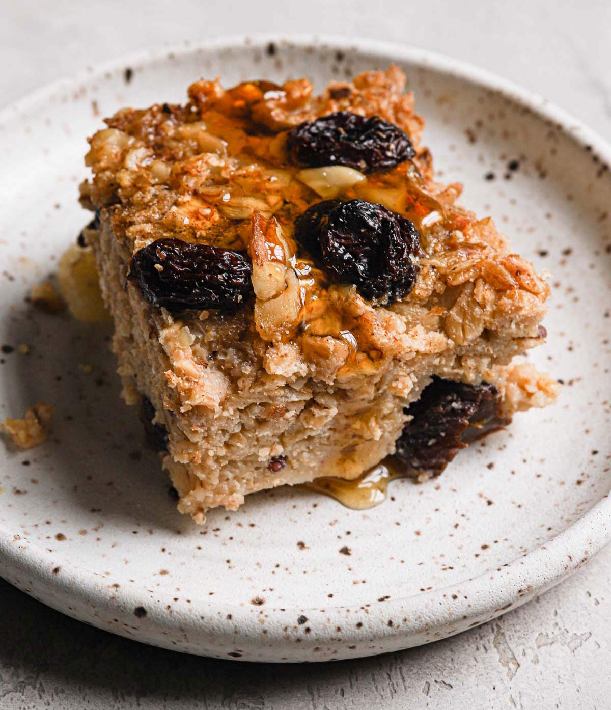 Square of baked oatmeal with apples, raisins, and walnuts on a plate.