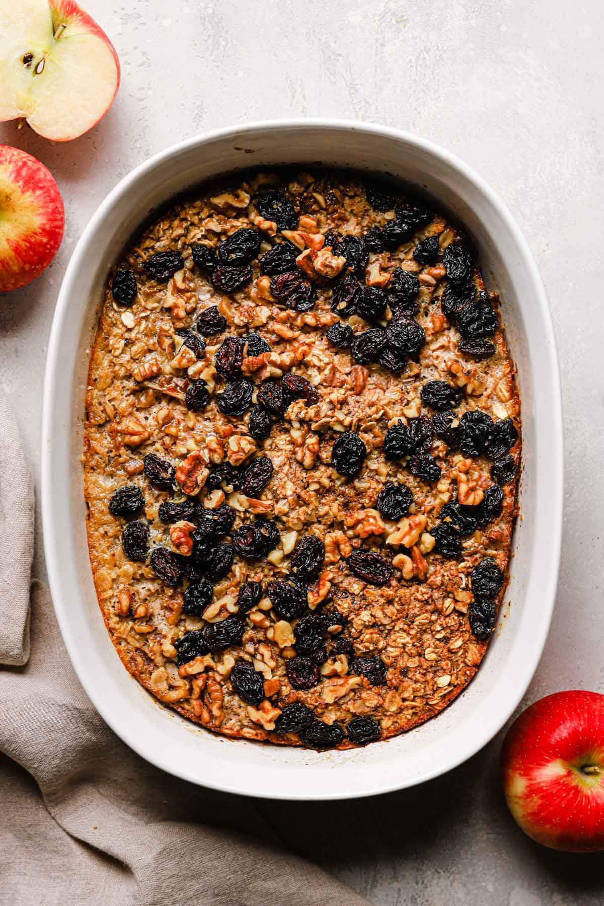 Healthy baked oatmeal in a white oval baking dish with apples, raisins and walnuts.